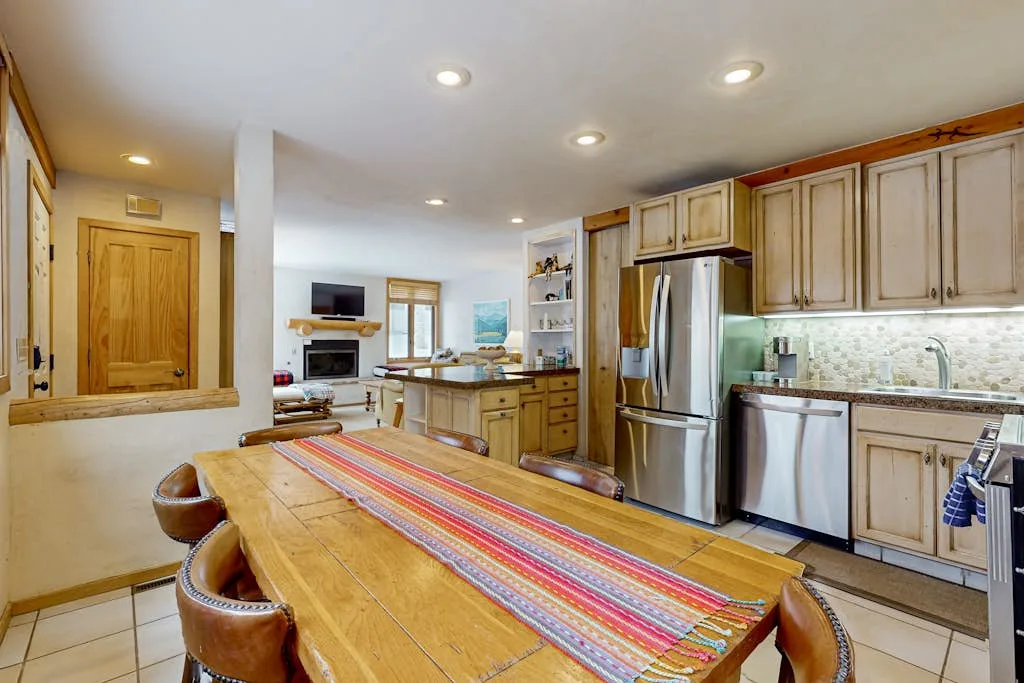 Cocina y comedor con una mesa larga de madera y un camino de mesa colorido.
