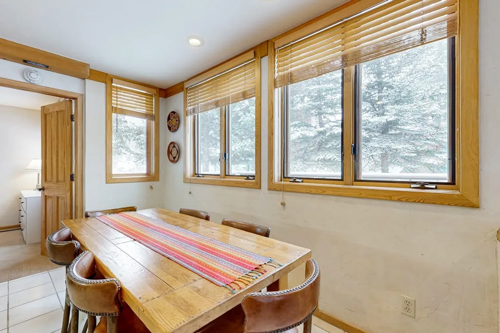 Un comedor con una mesa de madera y grandes ventanas con vista a árboles nevados.