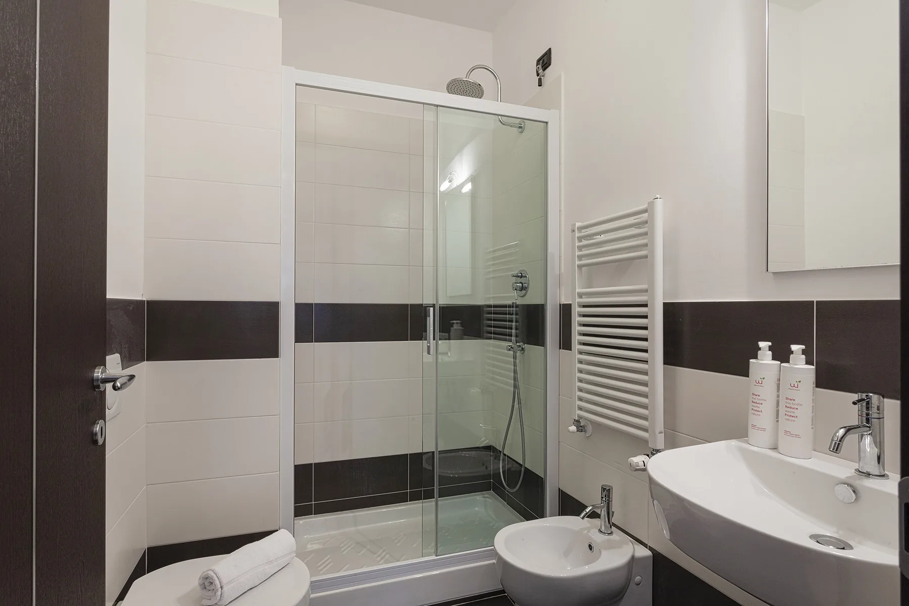 A tiled bathroom with a glass shower, sink, and bidet.