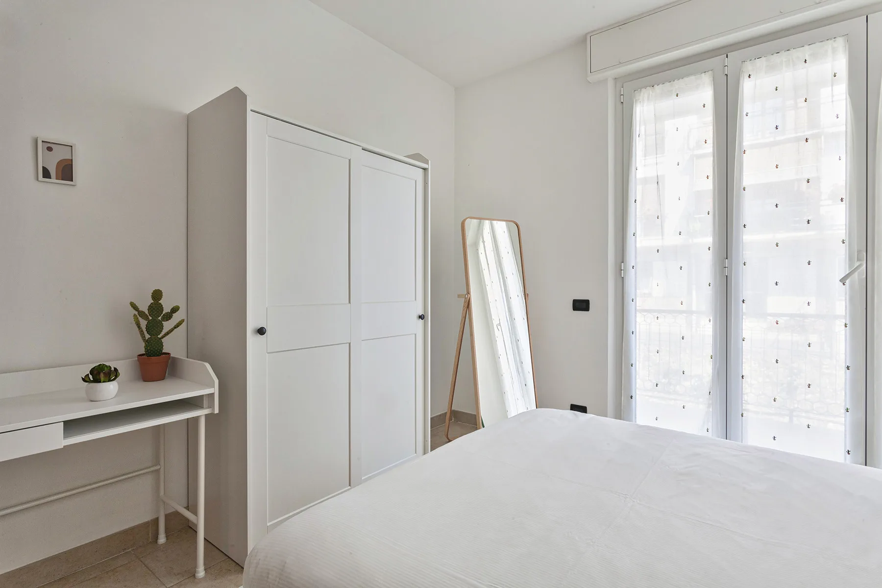 A bright bedroom with a bed, wardrobe, and tall windows.