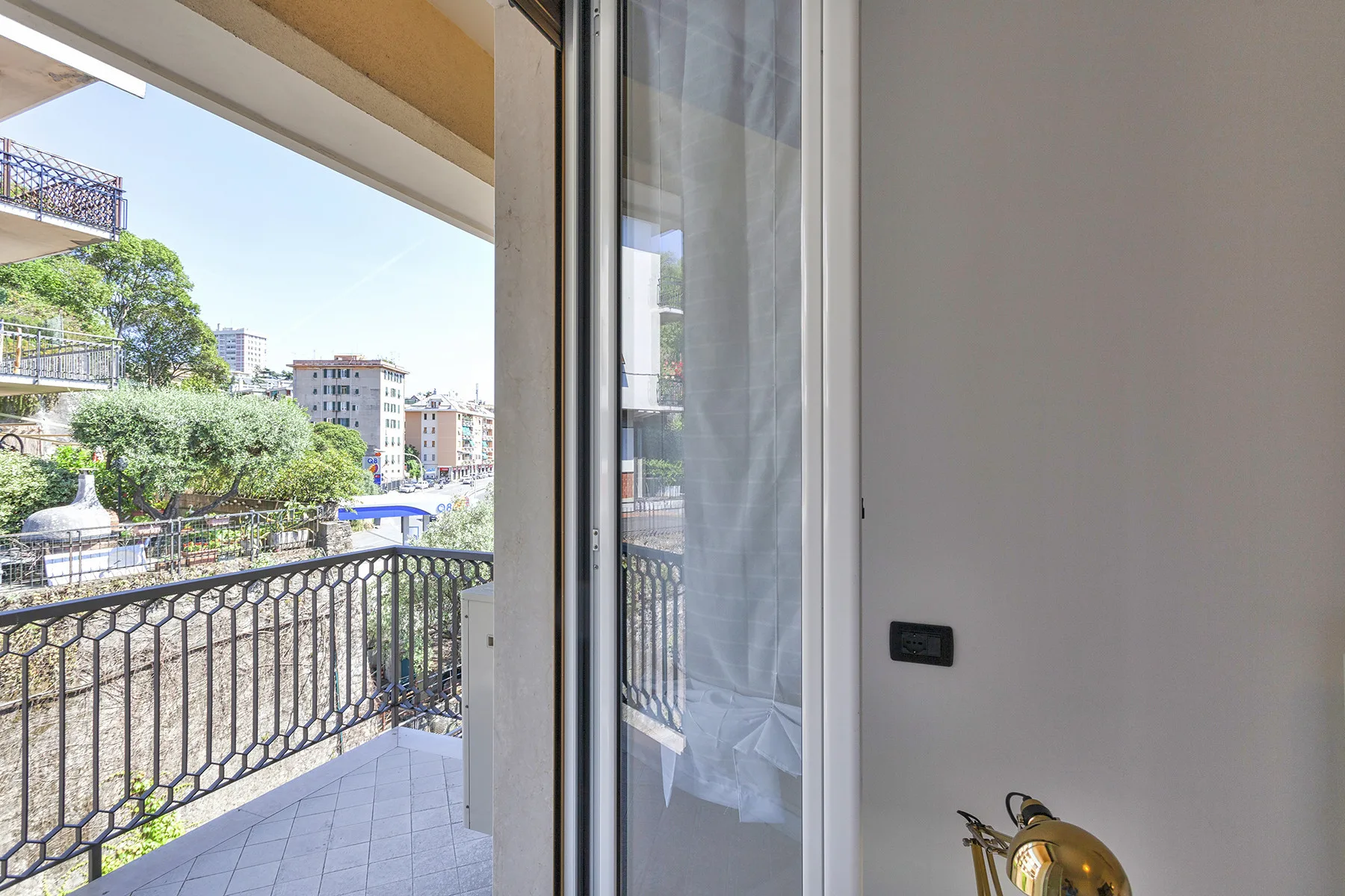 An open balcony beside a sliding glass door overlooks nearby buildings and trees.