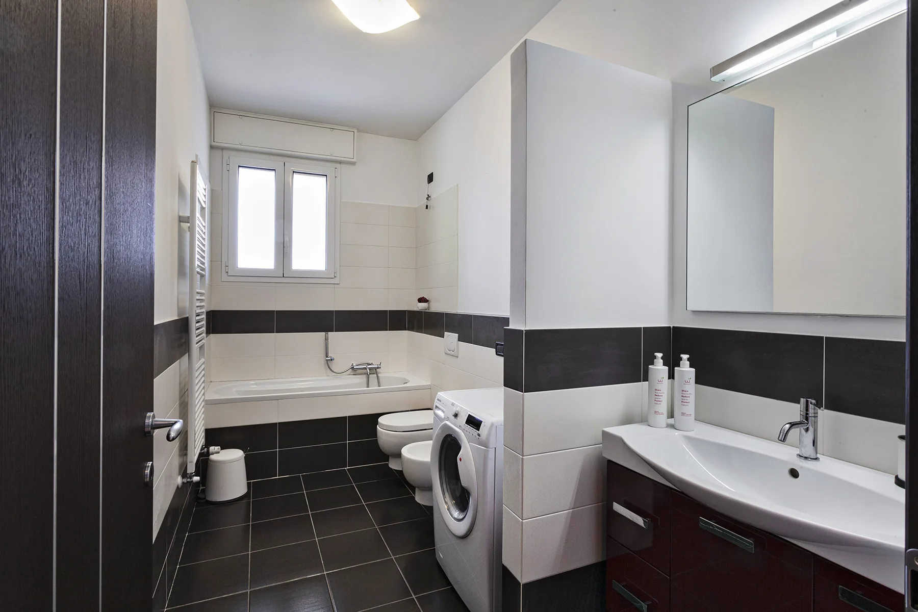 A bathroom with a bathtub, toilet, washing machine, and sink.