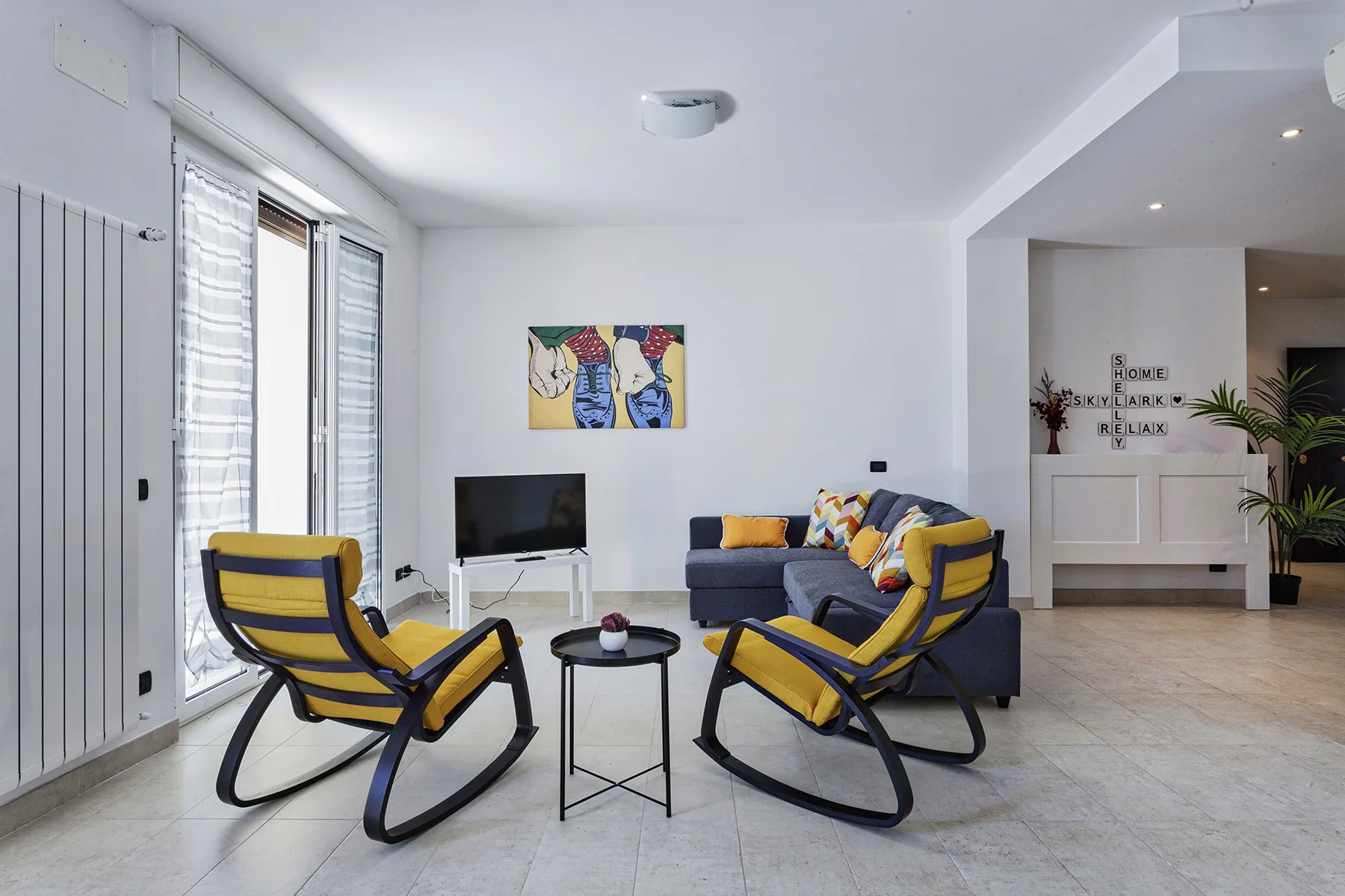 Una sala luminosa con asientos amarillos, un televisor y arte colorido en la pared.
