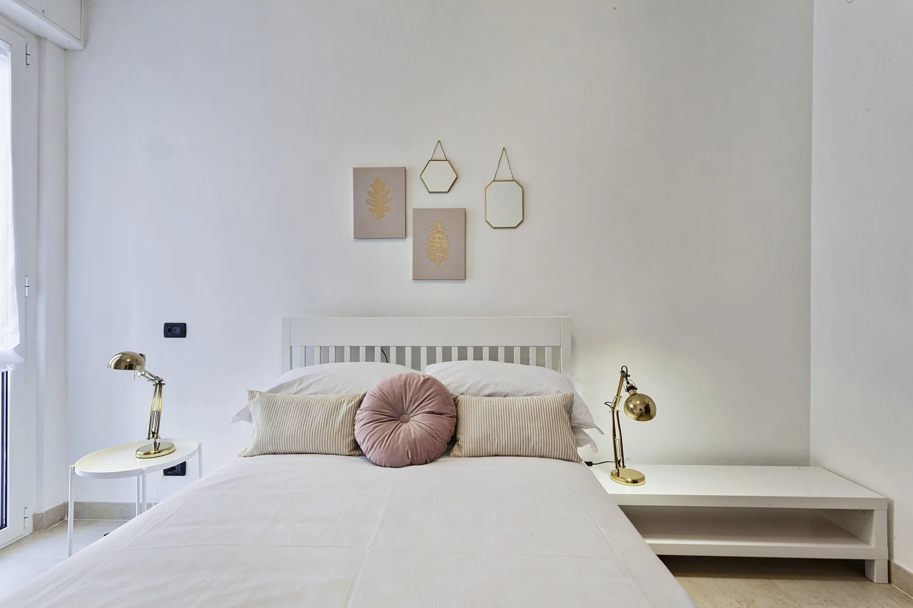 A bright bedroom features a neatly made bed and simple wall decorations.