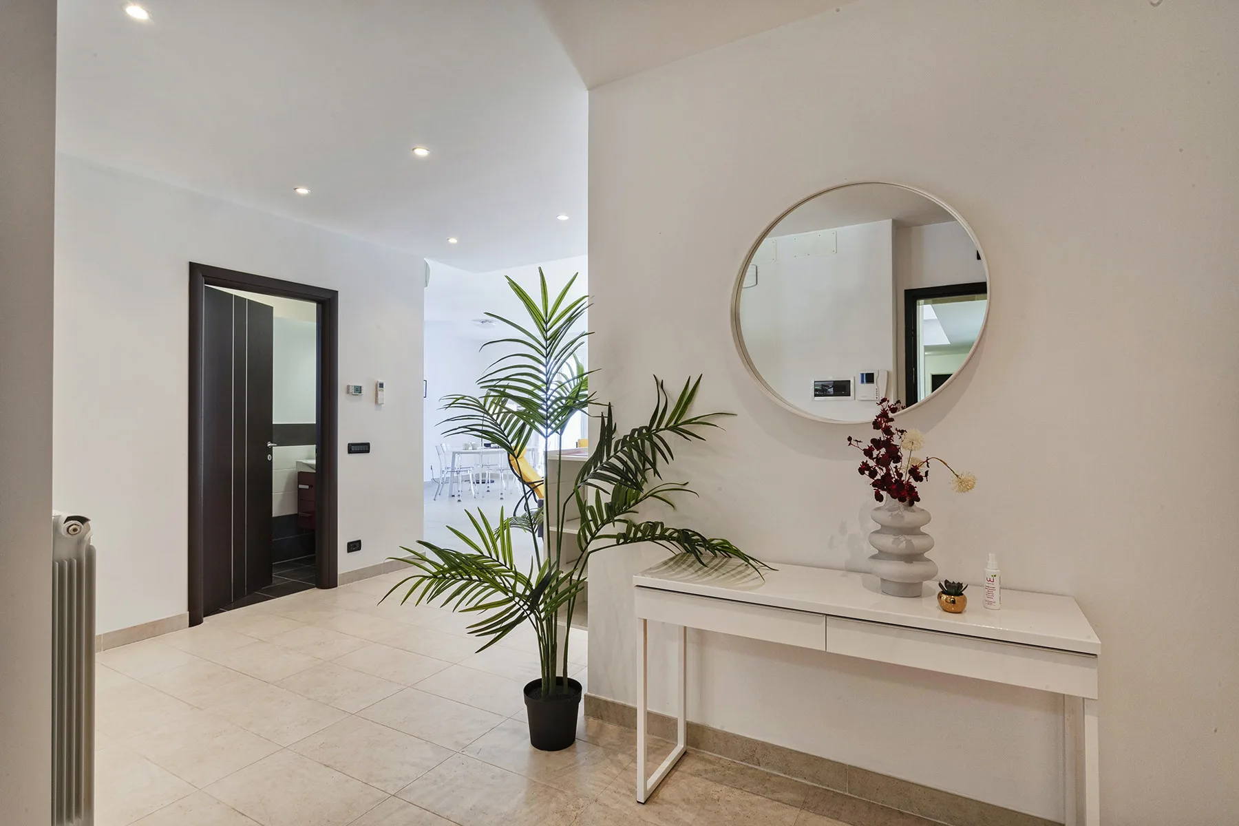 A bright entry hall with a console table, round mirror, and potted plants.