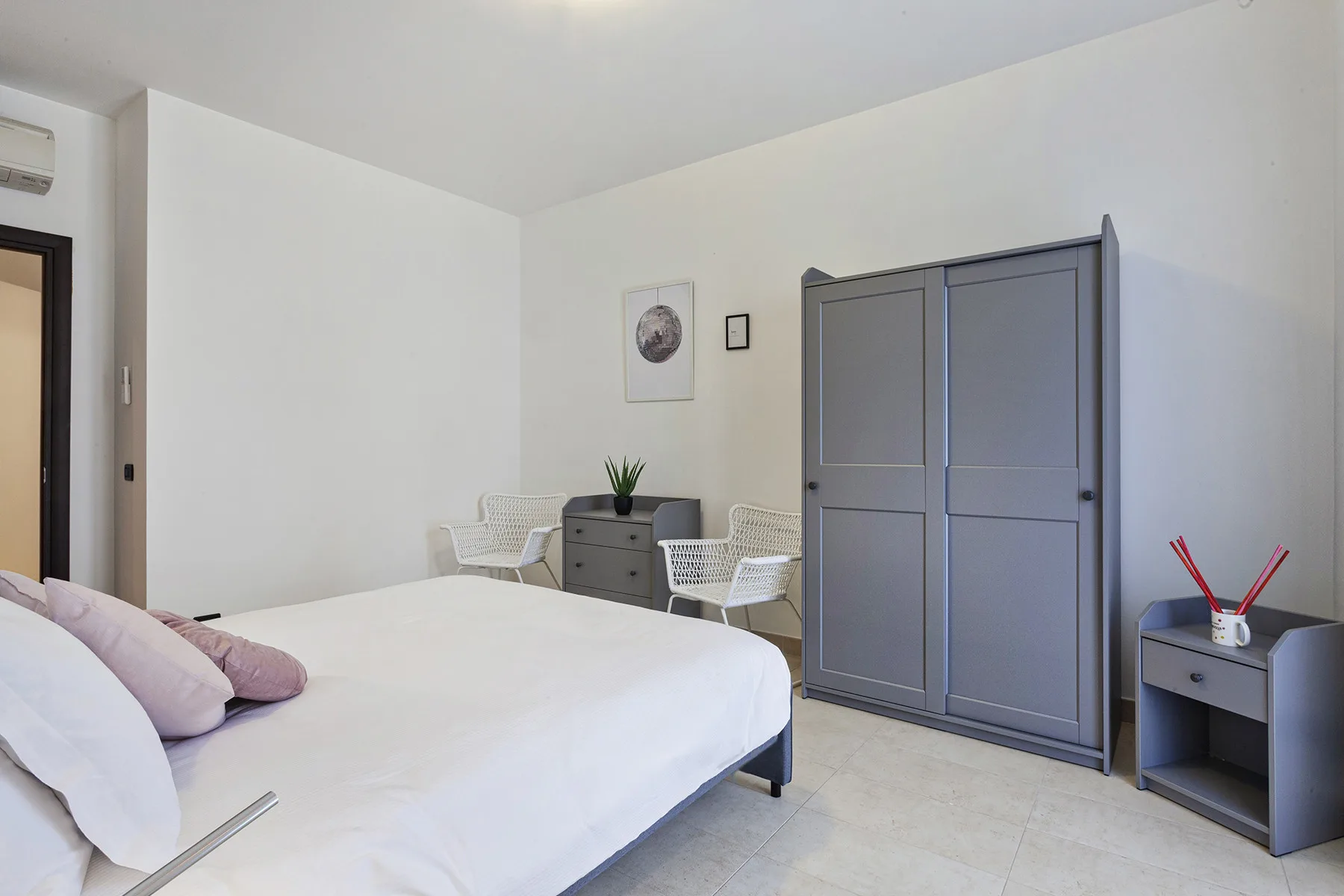 A bright bedroom with a bed, a wardrobe, and two chairs.