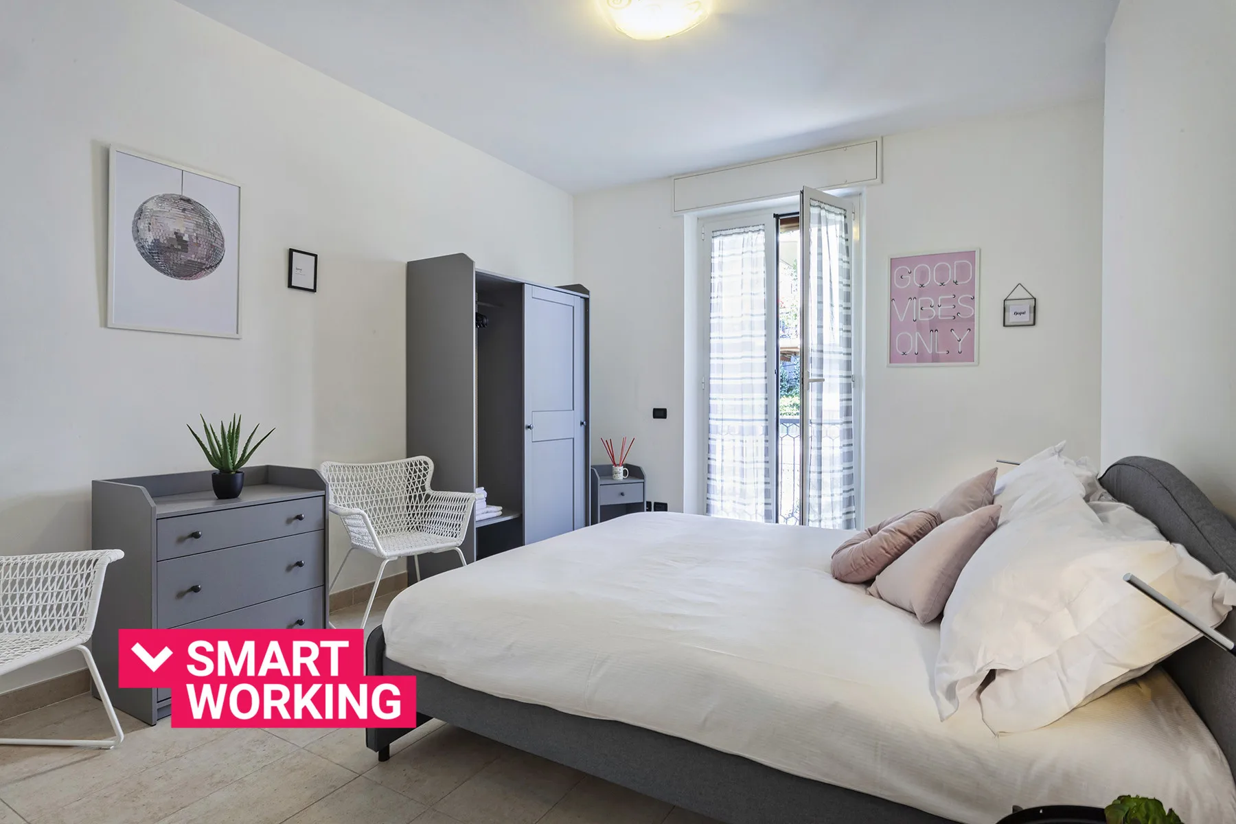 A bright bedroom with a large bed, a desk area, and a tall wardrobe.
