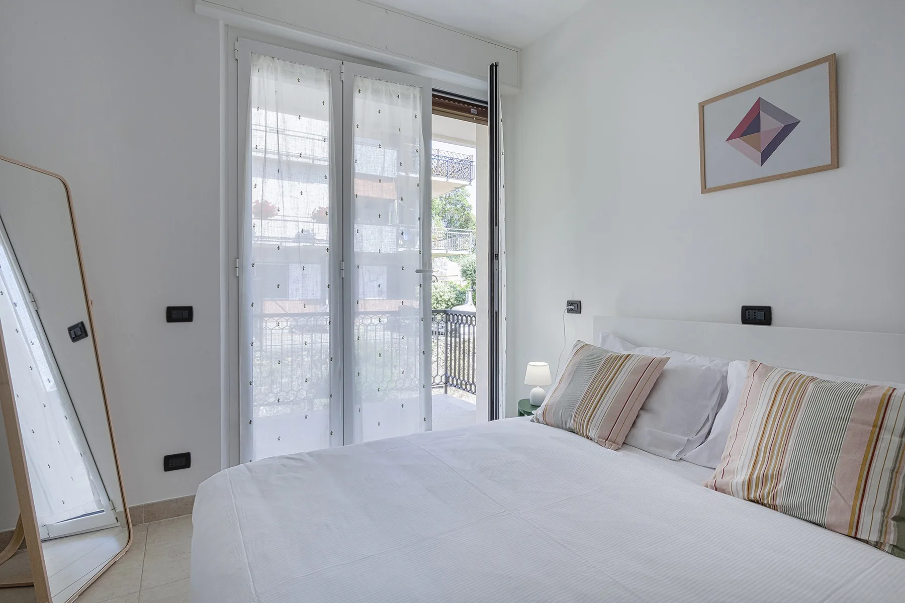 A bright bedroom with a neatly made bed beside a large window.