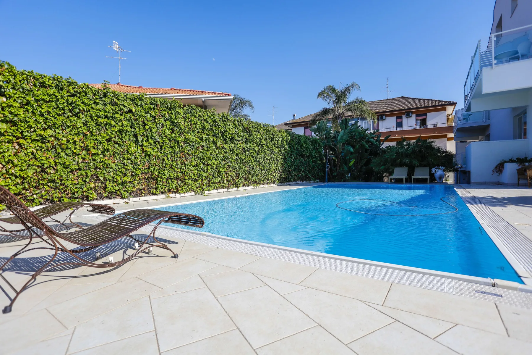 Una piscina al aire libre está rodeada por una terraza pavimentada y tumbonas.