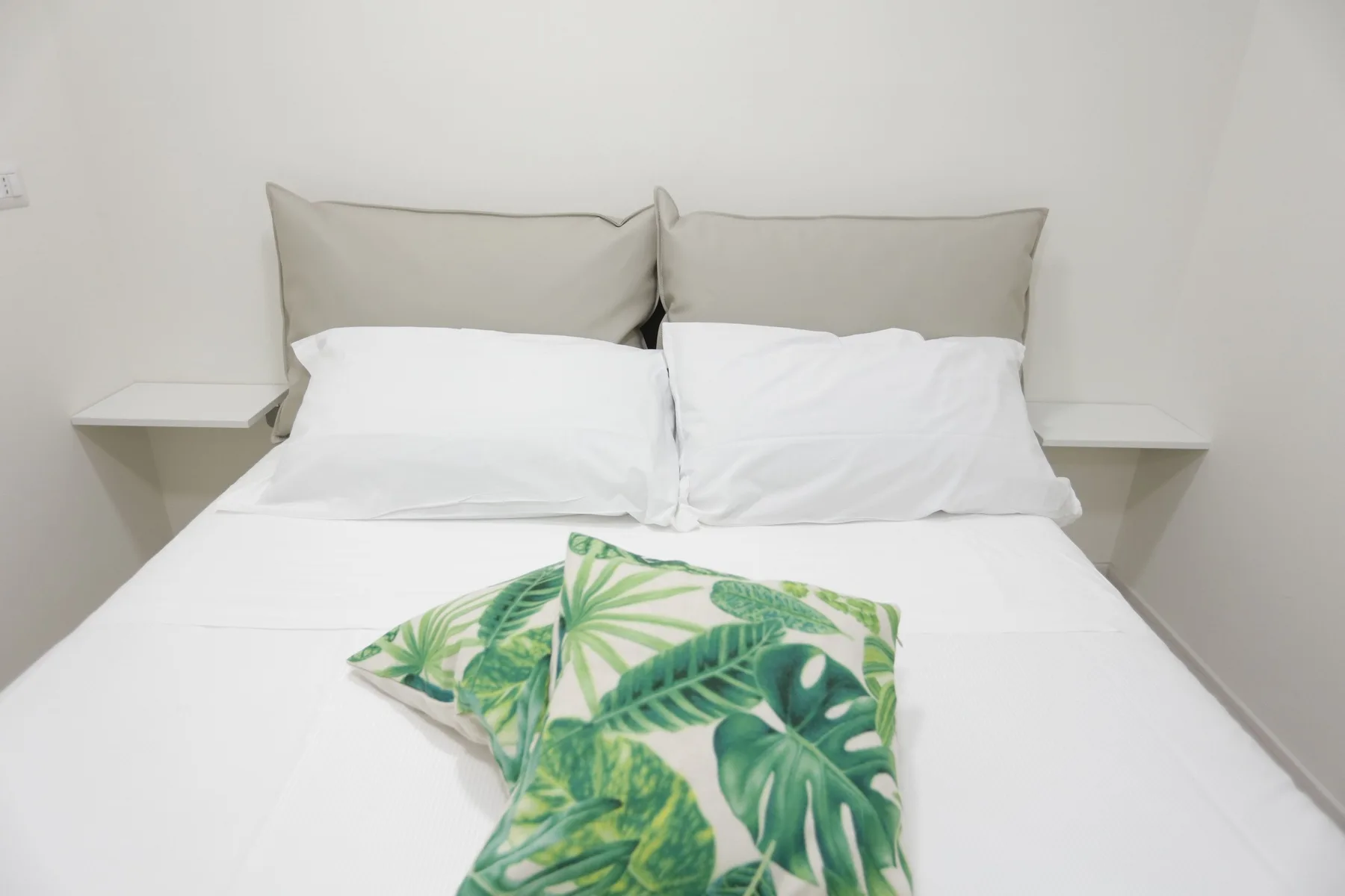 Un dormitorio con una cama blanca y ropa de cama con hojas verdes.