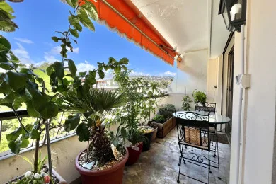 A plant-filled balcony with outdoor seating beneath an orange awning.