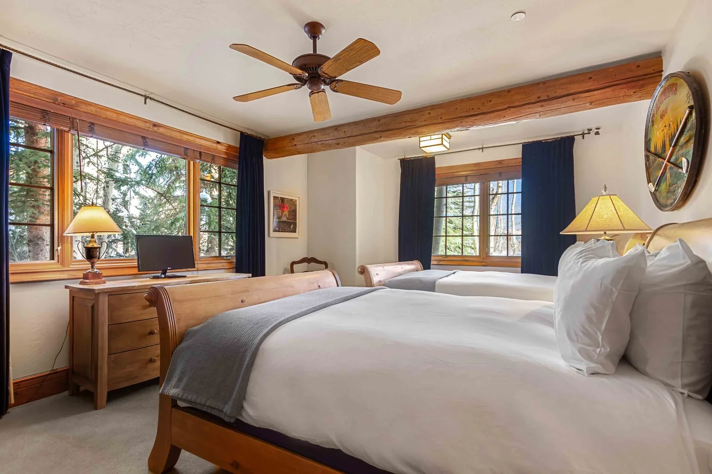 Un dormitorio con camas, muebles de madera y grandes ventanas con vista a los árboles.