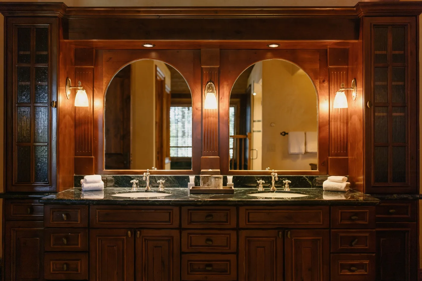 Un lavabo de baño con dos espejos, lavabos y muebles de madera oscura.