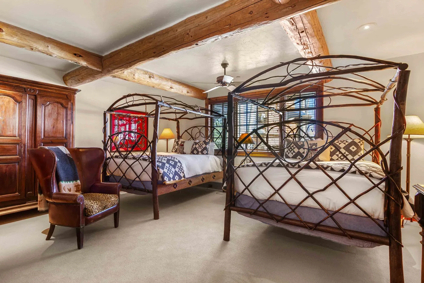 Dormitorio con dos camas ornamentadas, vigas de madera en el techo y un armario alto.