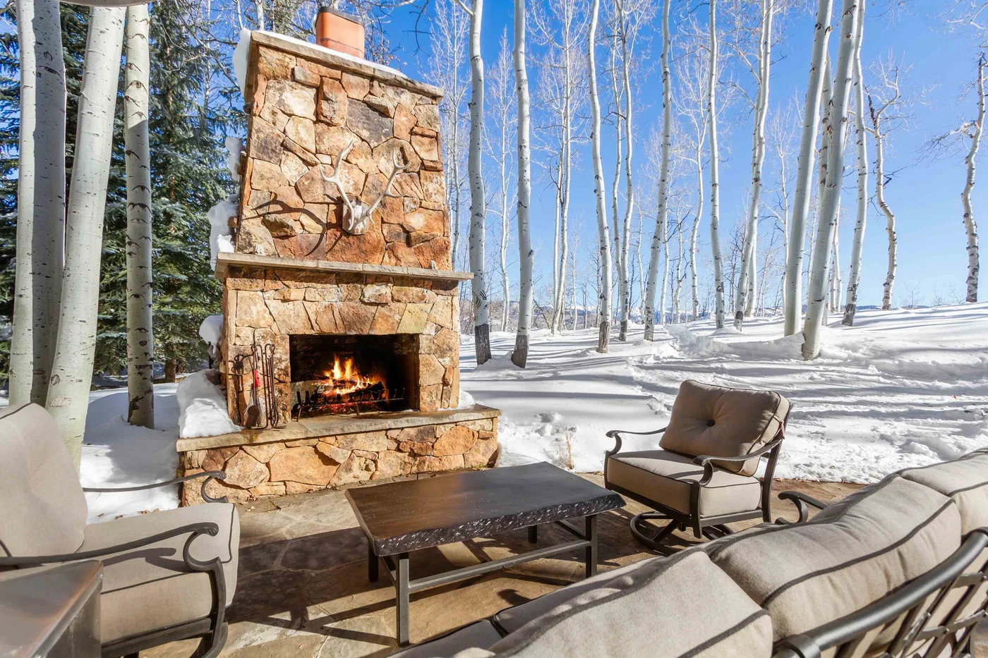 Una zona de estar al aire libre con una chimenea de piedra y árboles cubiertos de nieve.