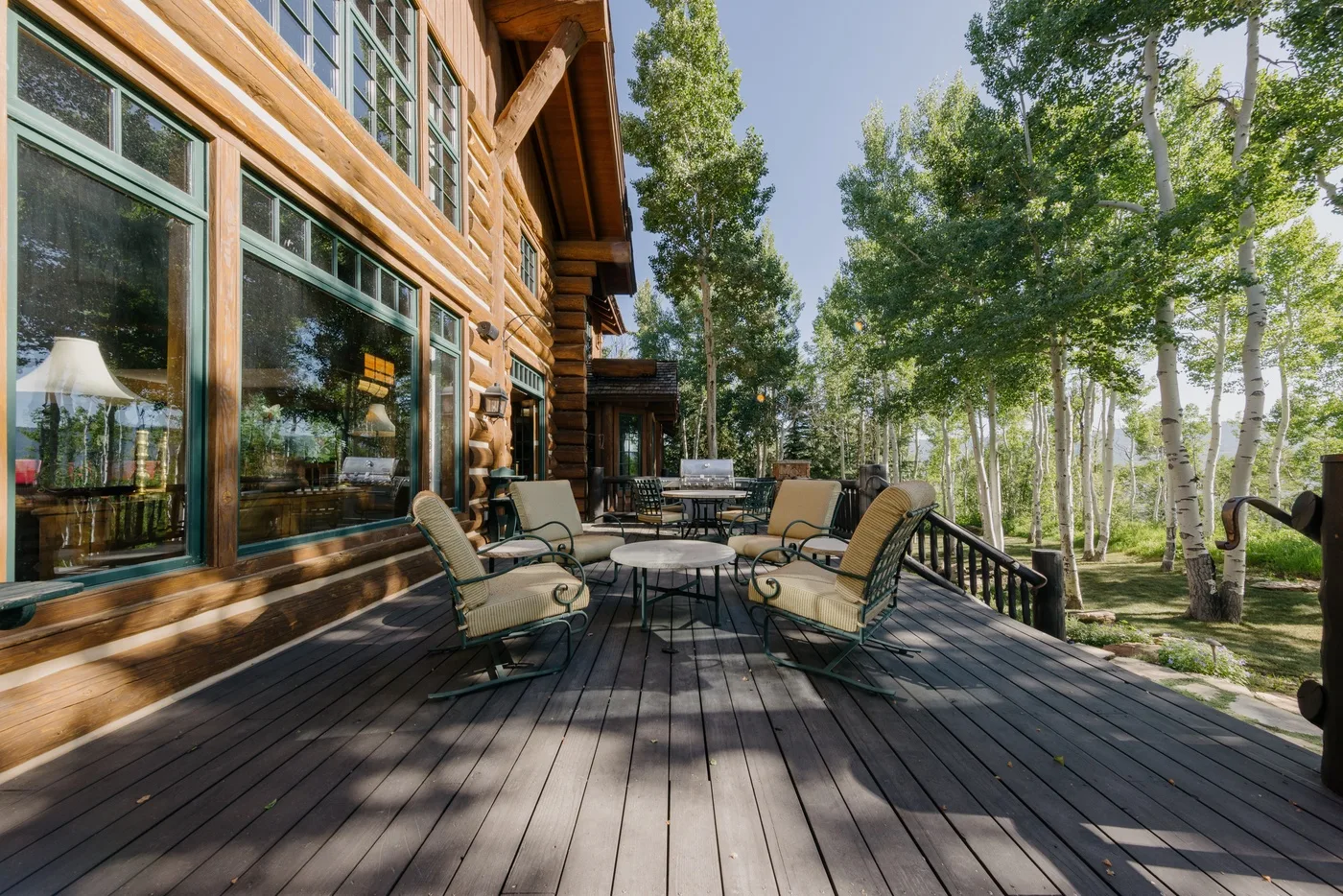 Una terraza de madera con asientos al aire libre junto a una casa de madera y árboles frondosos.