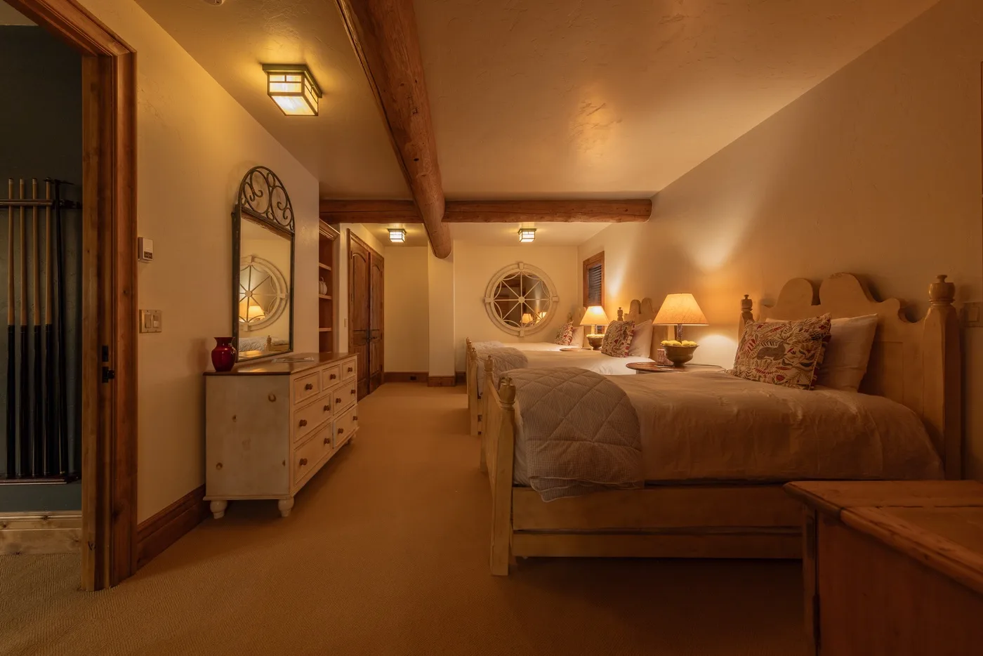 Un dormitorio con luz cálida, una cama grande y una cómoda junto a la puerta.