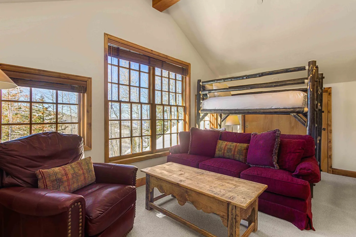 Una sala de estar con asientos color burdeos, una mesa de centro de madera y ventanas grandes.