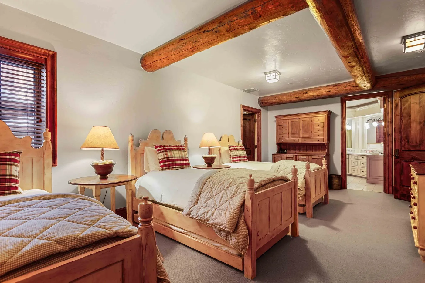 Un dormitorio con varias camas de madera y lámparas junto a la cama, bajo vigas expuestas.