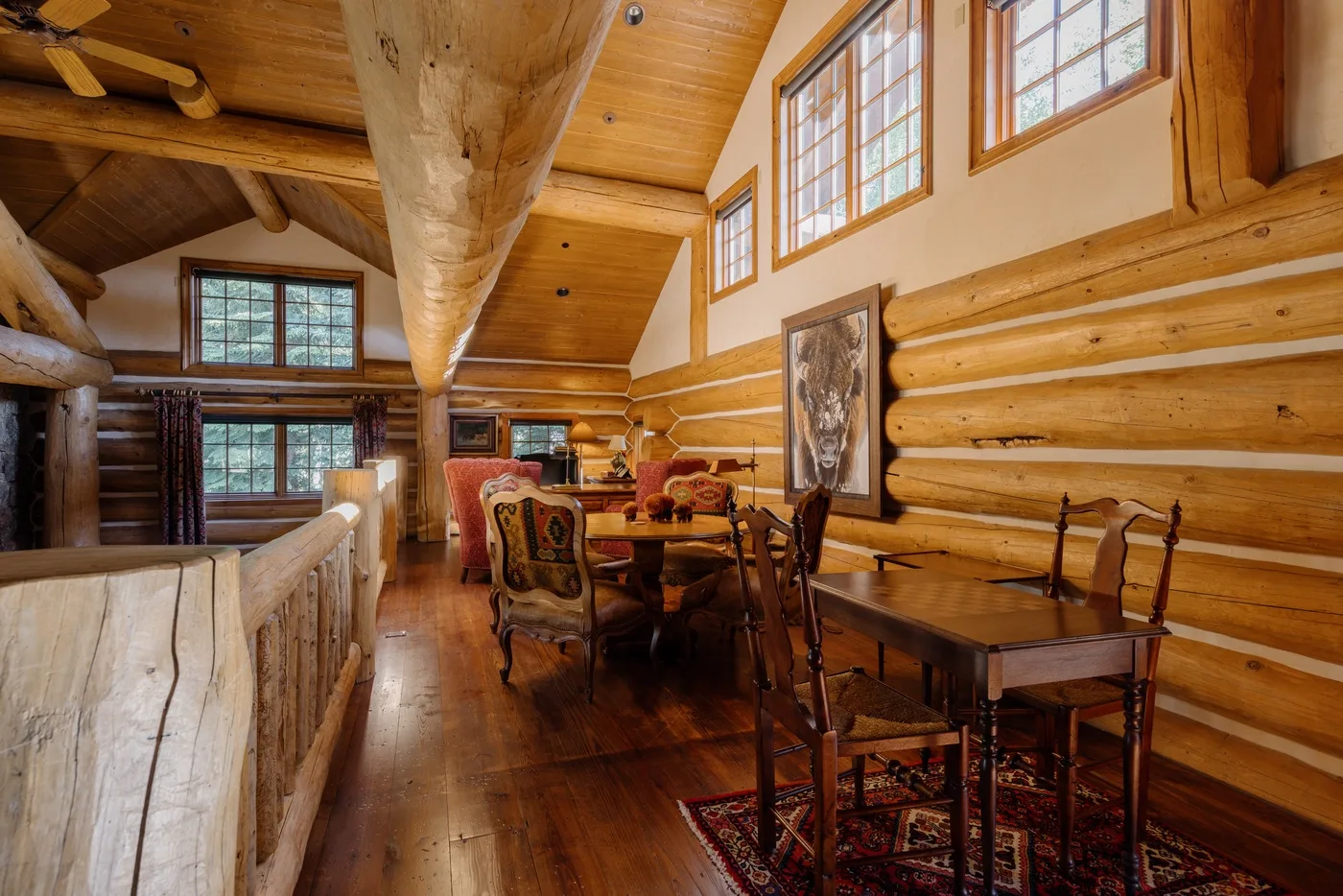 Comedor de una cabaña de troncos con mesas de madera y ventanas grandes.