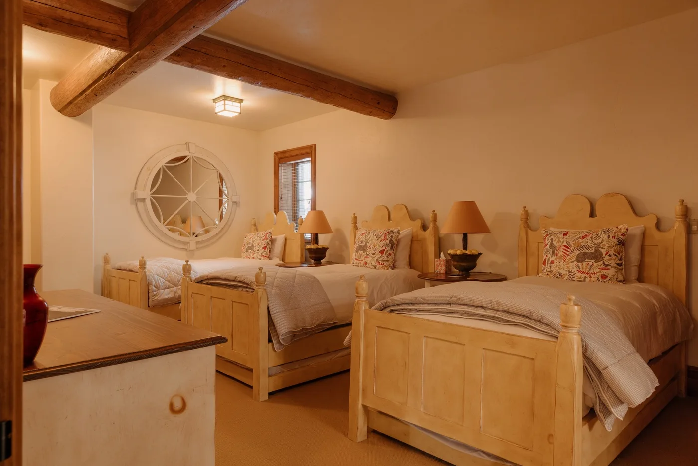 Un dormitorio de tonos cálidos con dos camas de madera y una ventana redonda.