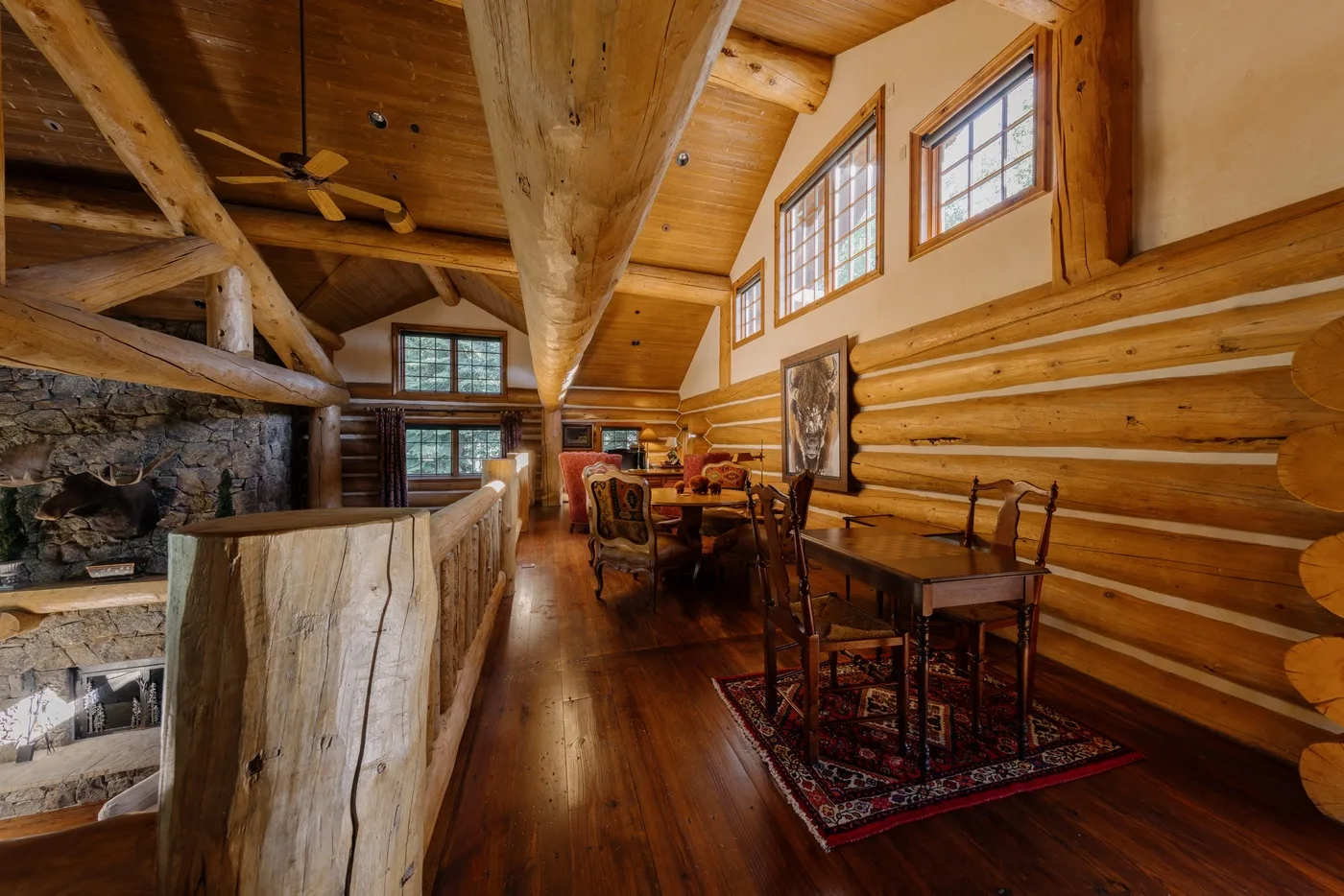 Un comedor de cabaña de troncos con mesas de madera bajo ventanas altas.