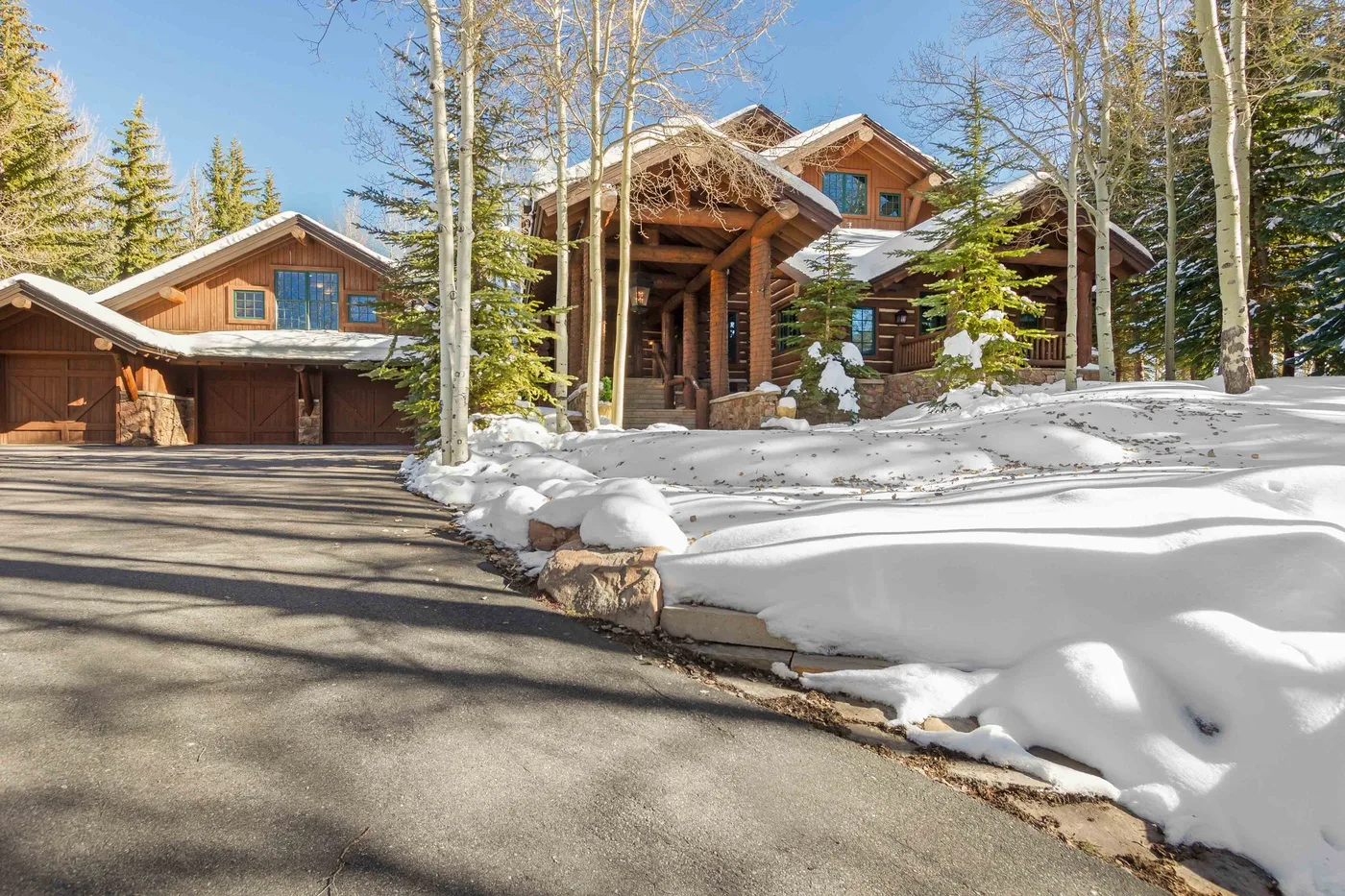 Una casa grande de madera está junto a una entrada nevada y árboles.