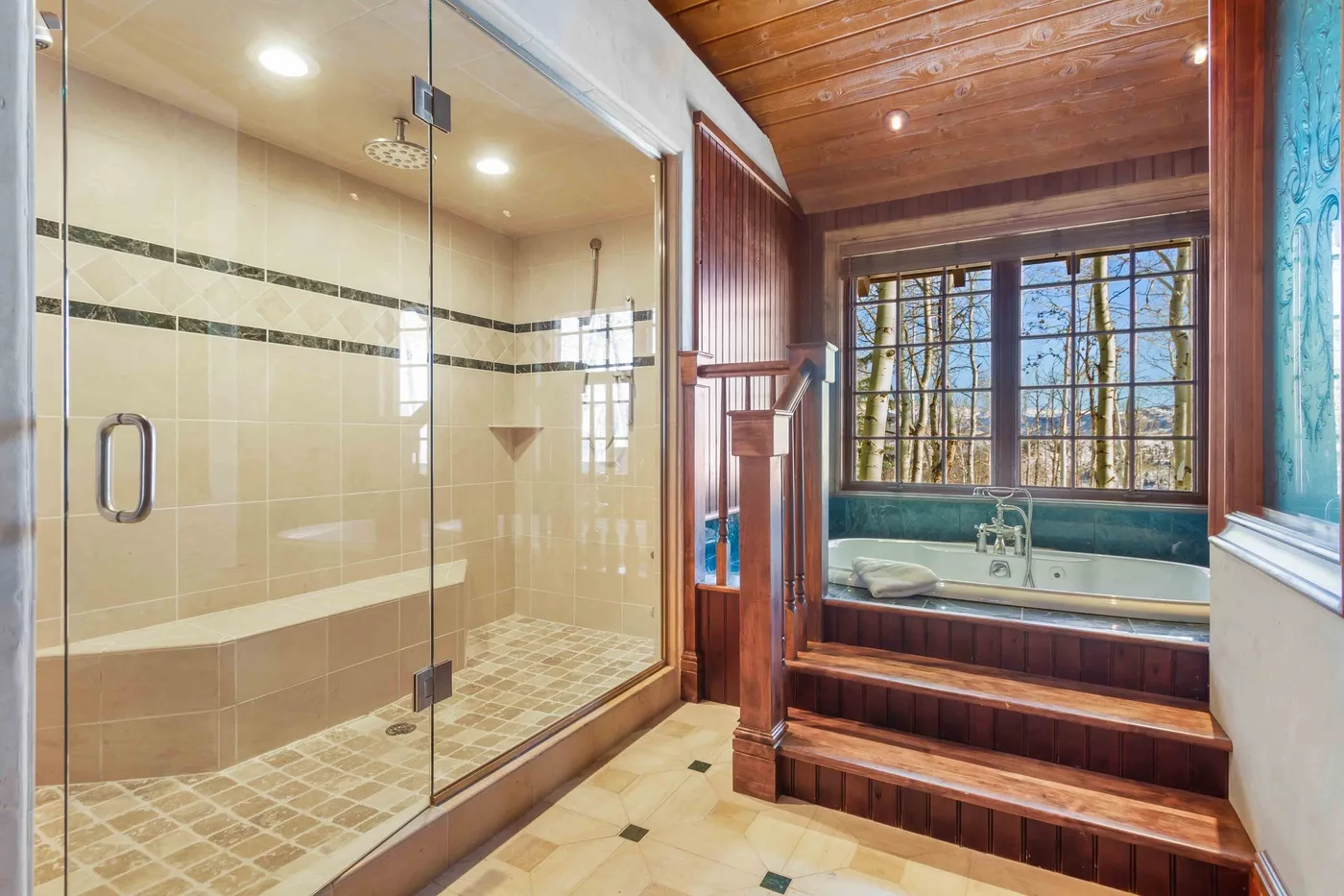 Un baño con ducha de vidrio junto a una bañera empotrada bajo grandes ventanas.