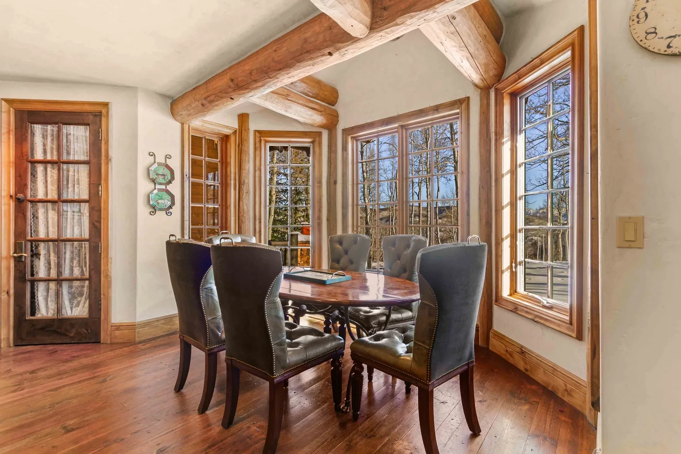 Un comedor con una mesa de madera y asientos junto a grandes ventanas.