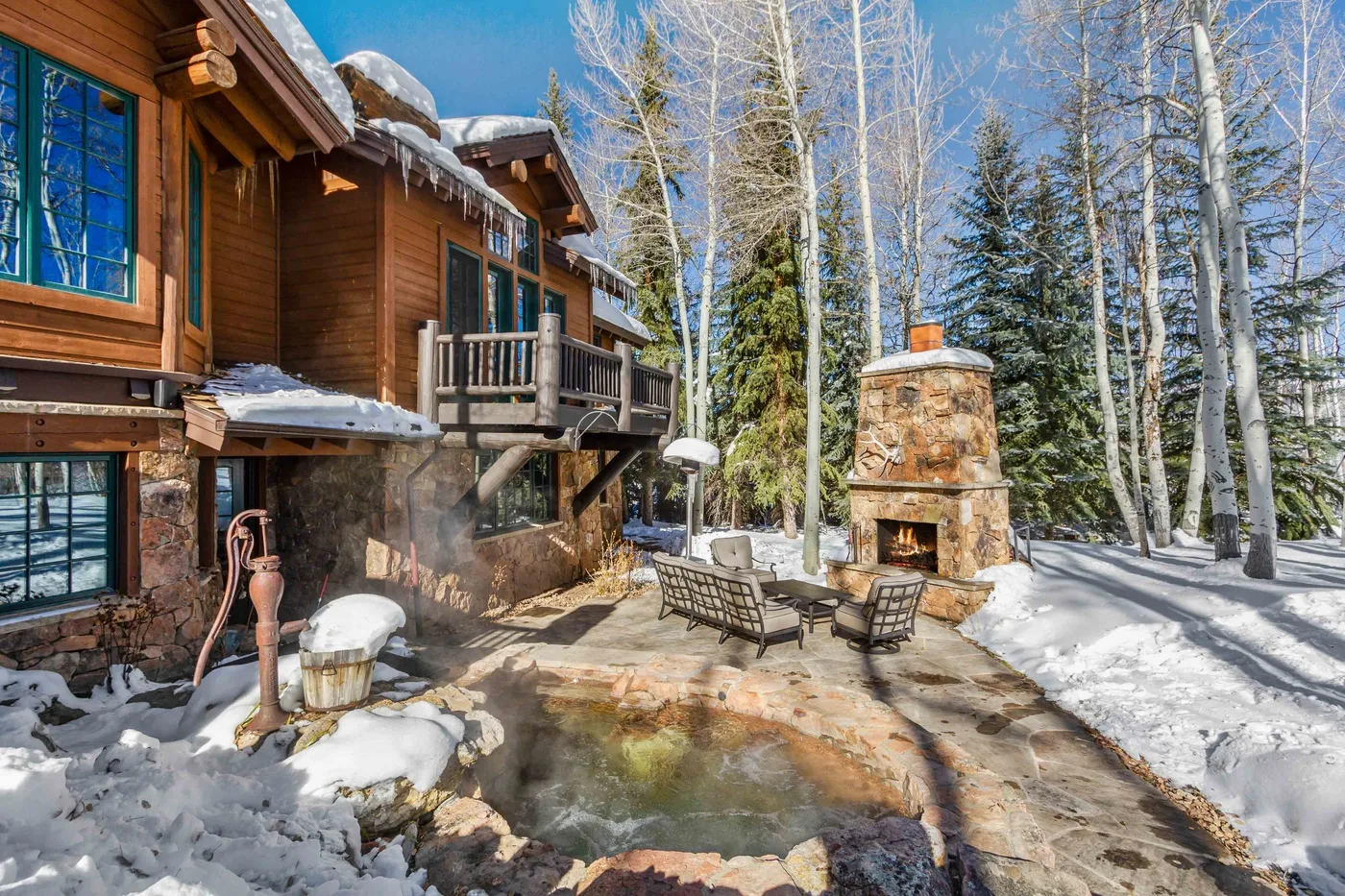 Un patio exterior nevado con asientos y una chimenea de piedra junto a un edificio de madera.