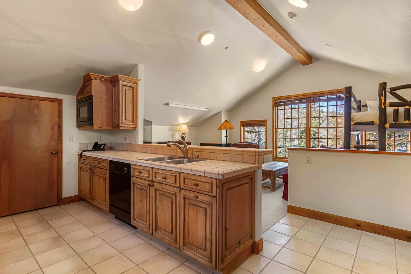 Una cocina con gabinetes de madera, una encimera de azulejos y ventanales.