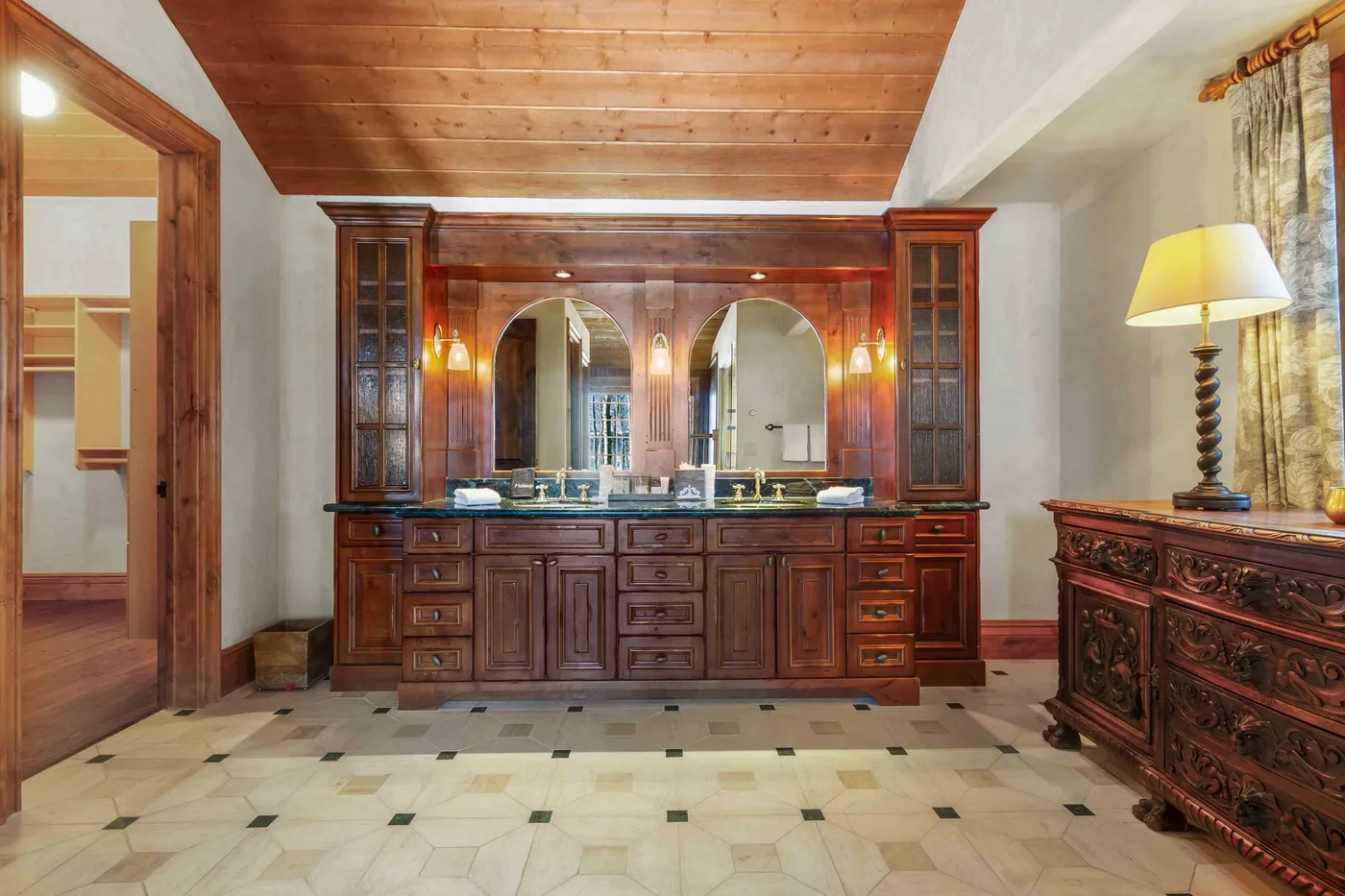 Un baño con un largo tocador de madera y dos espejos bajo un techo revestido de madera.