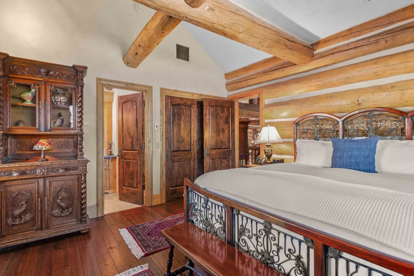 Un dormitorio con una cama grande, vigas de madera a la vista y muebles de madera tallada.