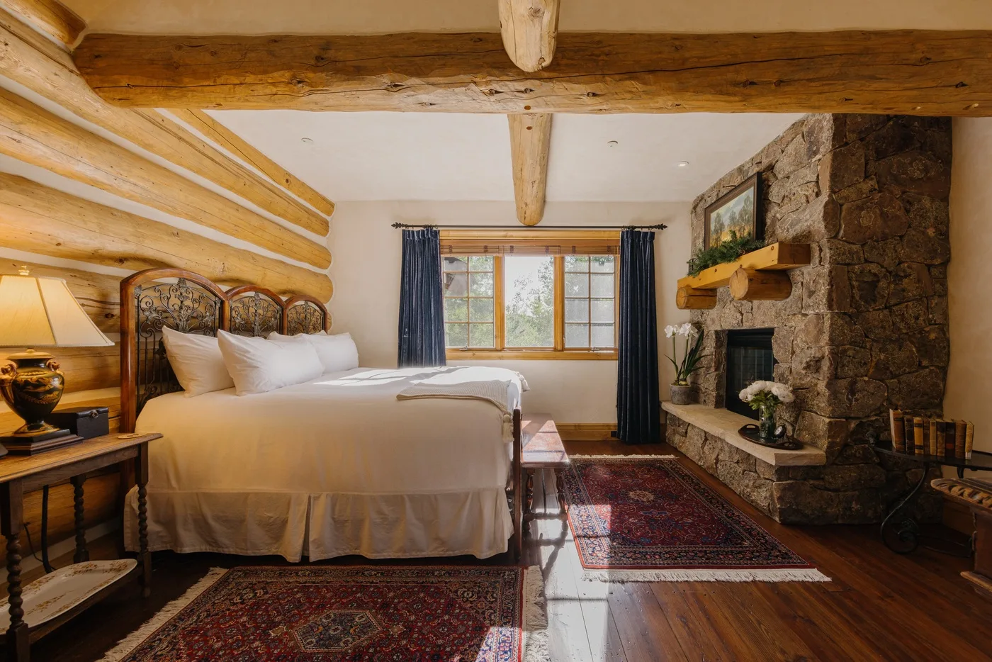 Un dormitorio con una cama, vigas de madera, una ventana y una chimenea de piedra.