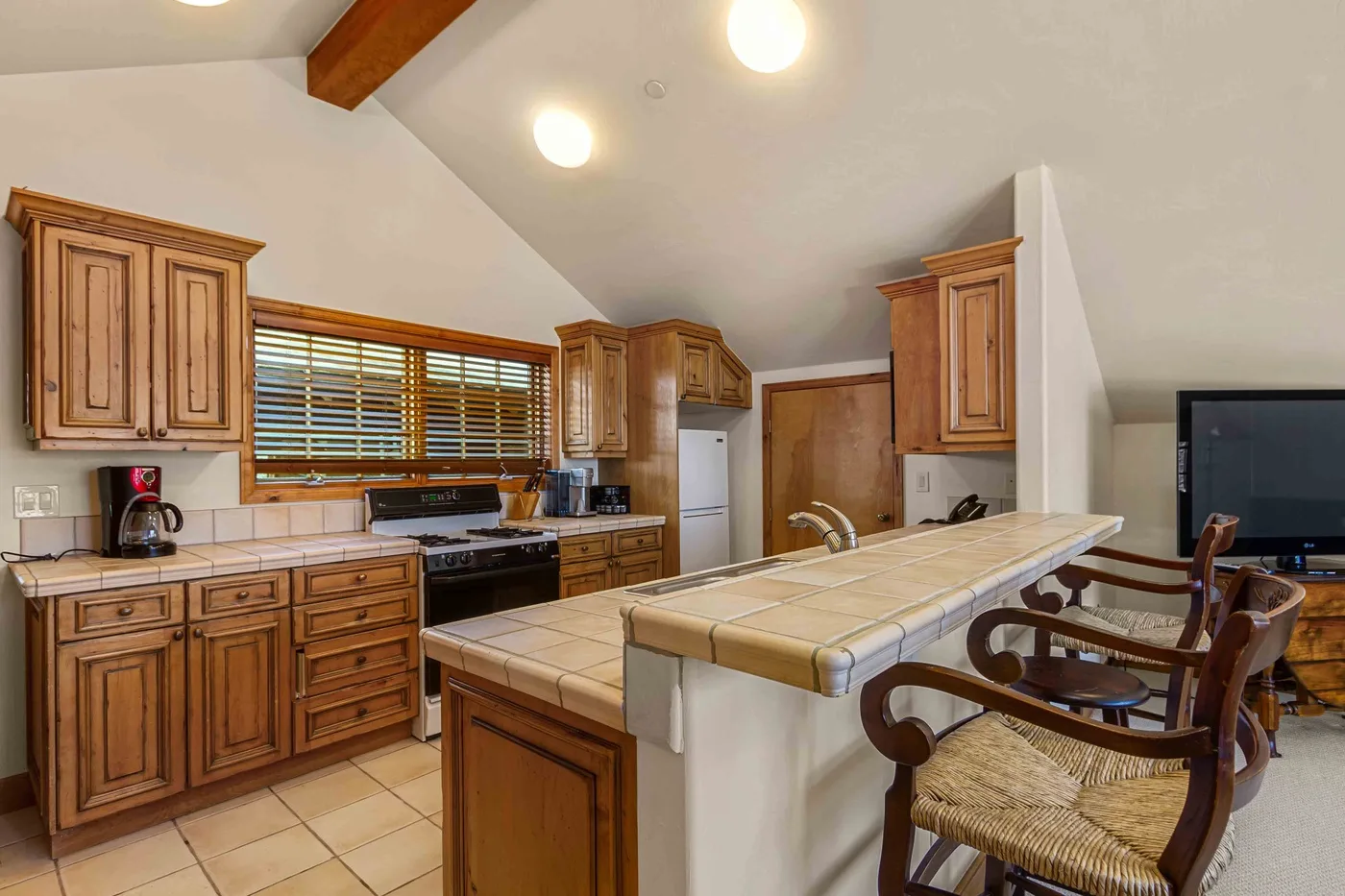 Una cocina con gabinetes de madera, encimeras de azulejos y una barra de desayuno.