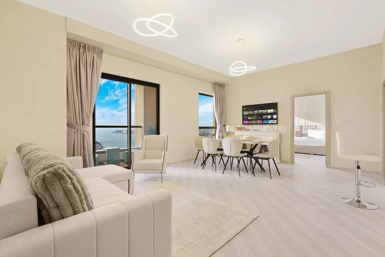 A bright living and dining area has seating beside large windows and a dining table.