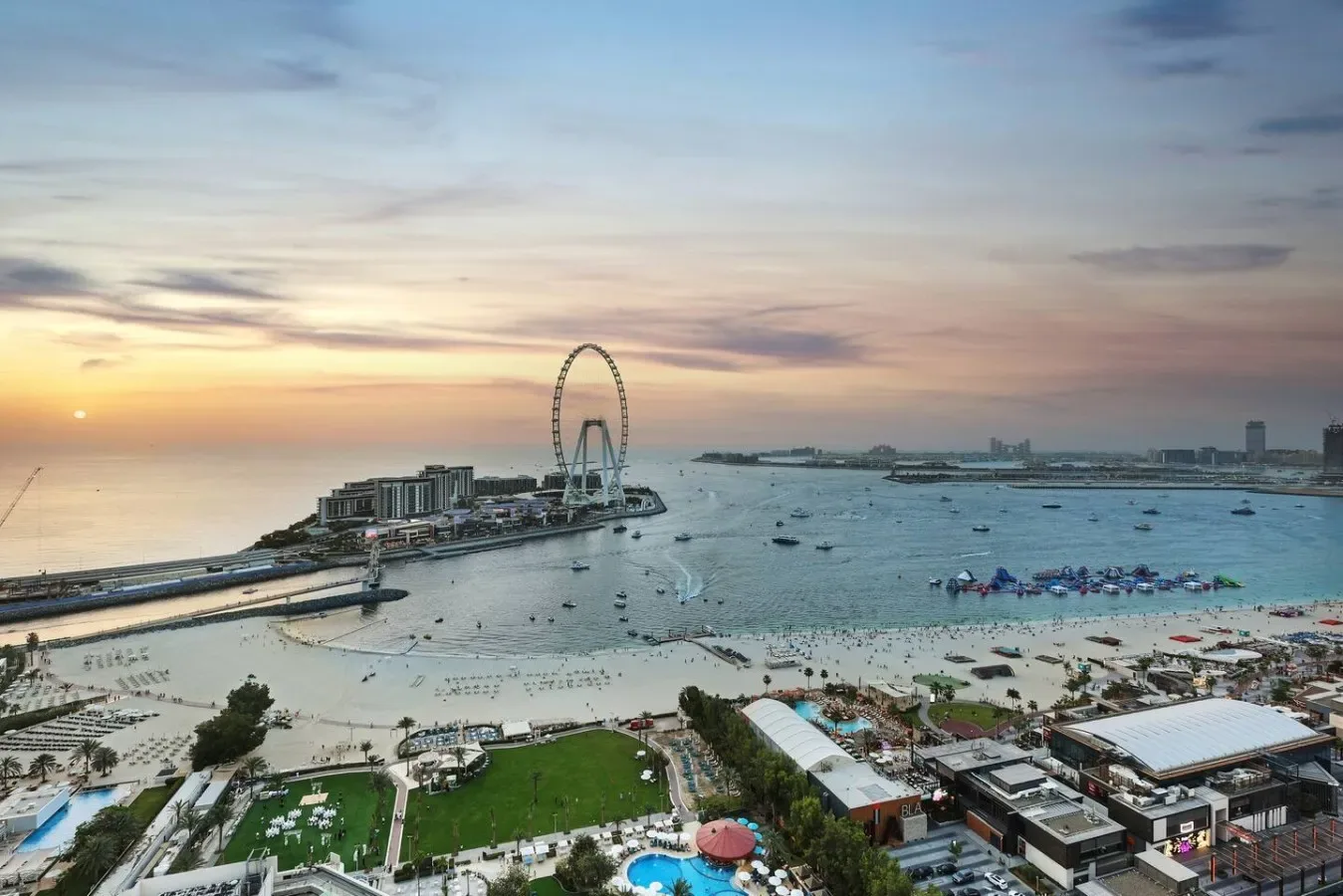 A coastal waterfront at sunset, with a large observation wheel beside the beach.