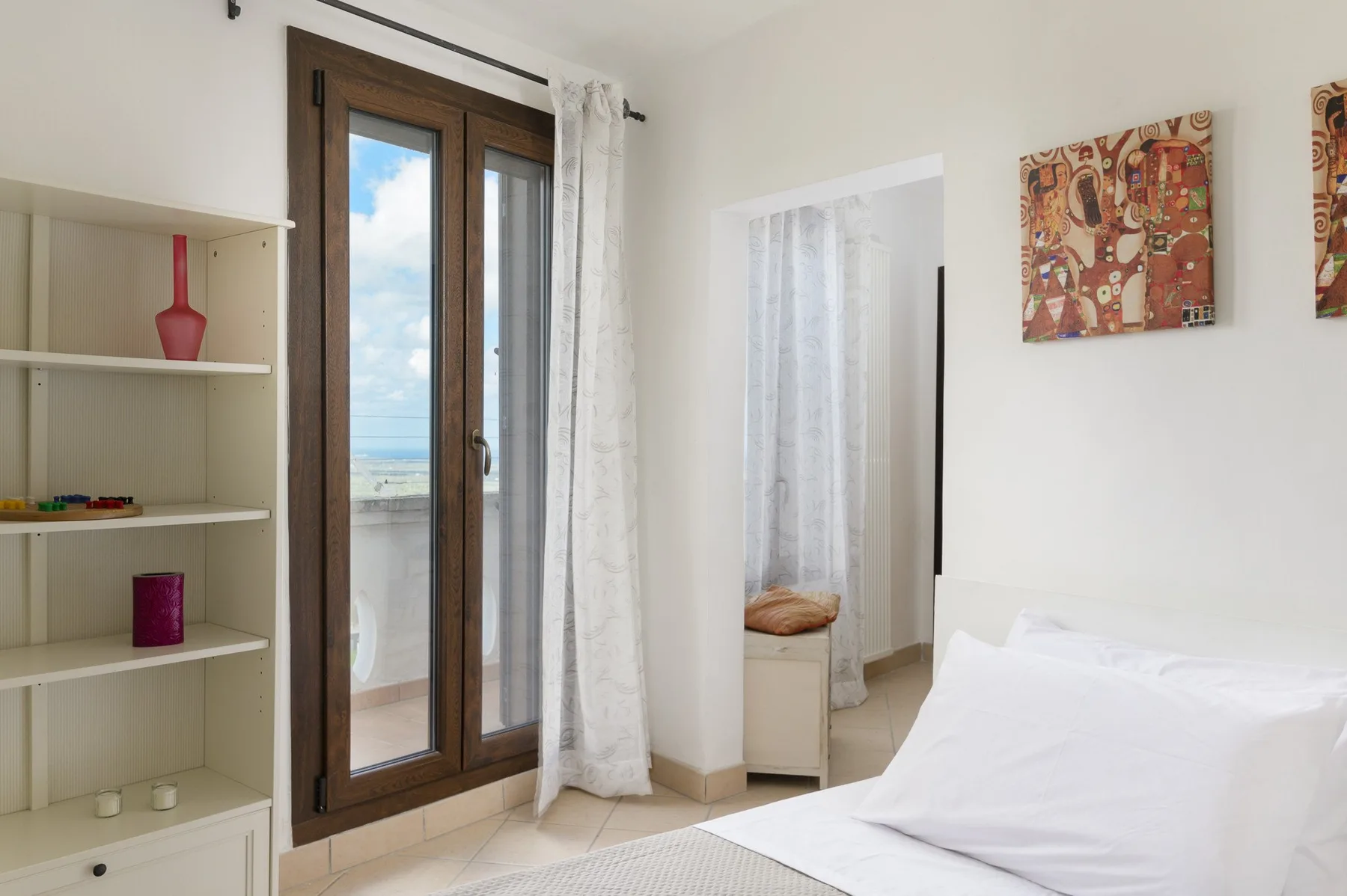 Un dormitorio luminoso con cama, ventana alta y estanterías empotradas.