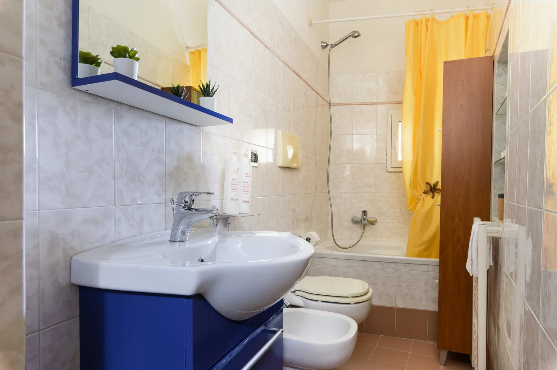 Un baño alicatado con lavabo, inodoro y cortina de ducha amarilla.