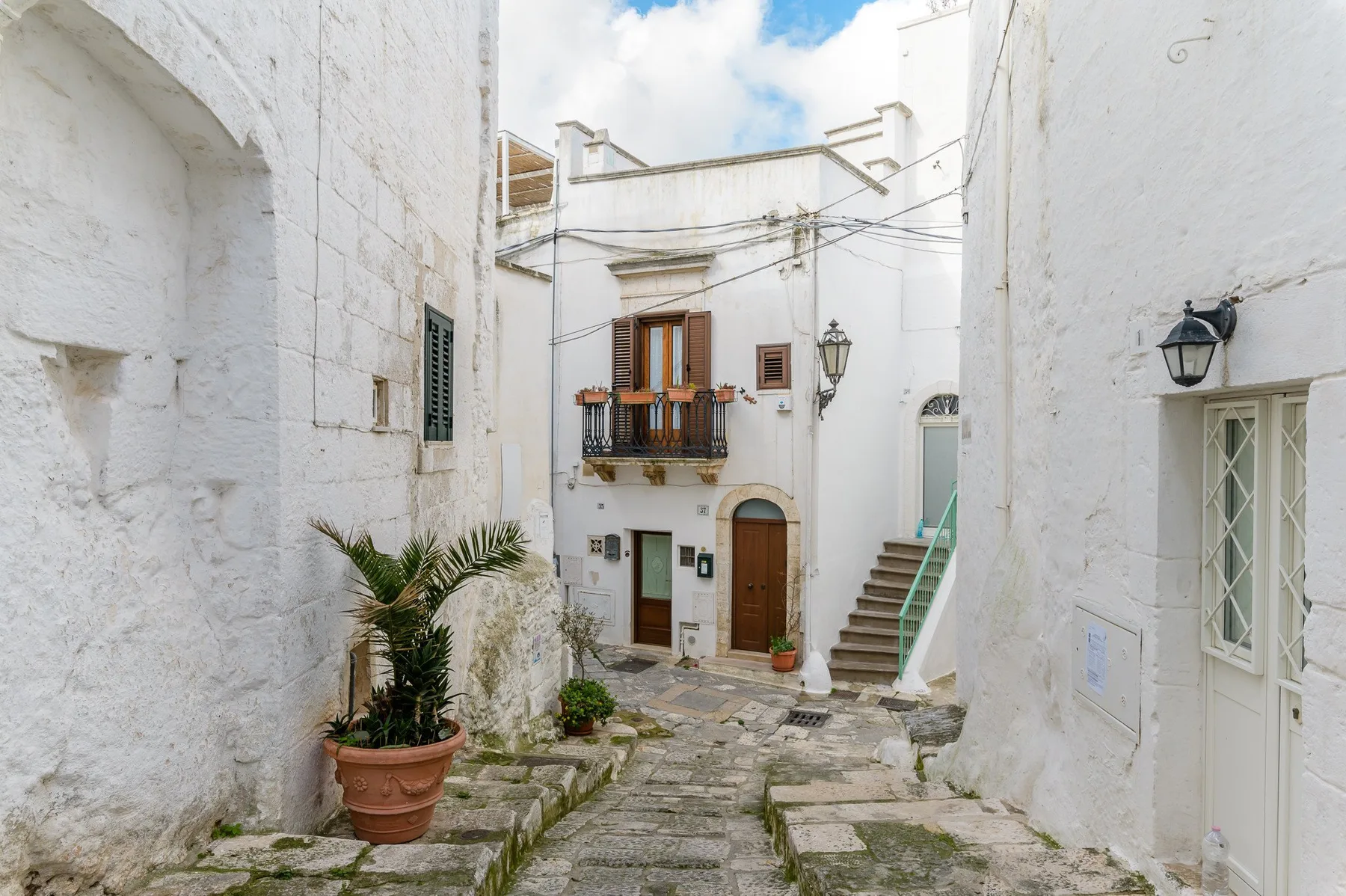 Un estrecho patio empedrado está rodeado de edificios blancos y plantas en macetas.