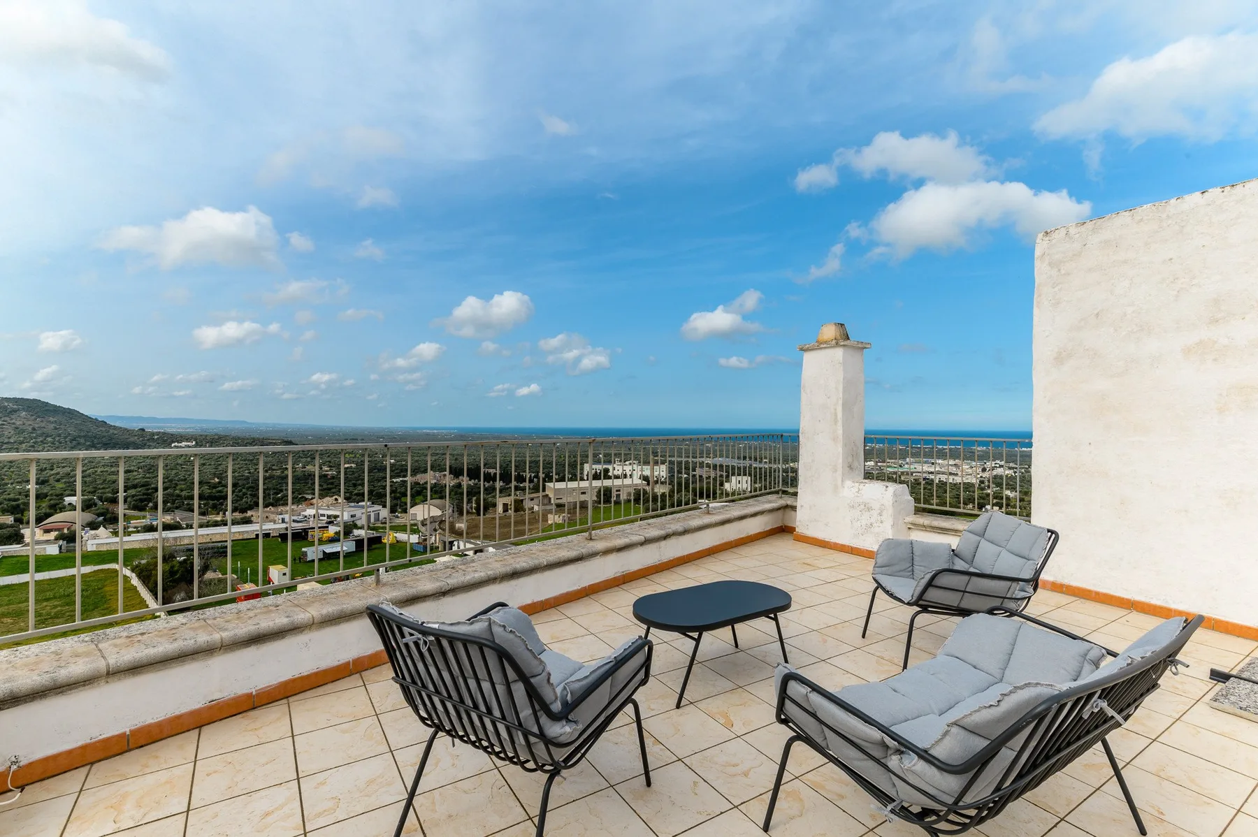 Una terraza de baldosas tiene asientos acolchados y una amplia vista de la costa.