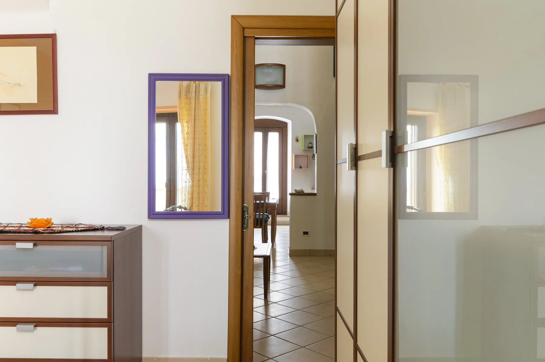 Una puerta del dormitorio da a un pasillo embaldosado con una ventana al fondo.