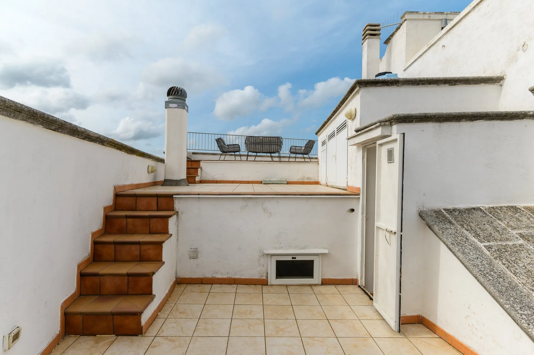 Una terraza en la azotea con suelo de baldosas y escalones hacia una zona de estar.