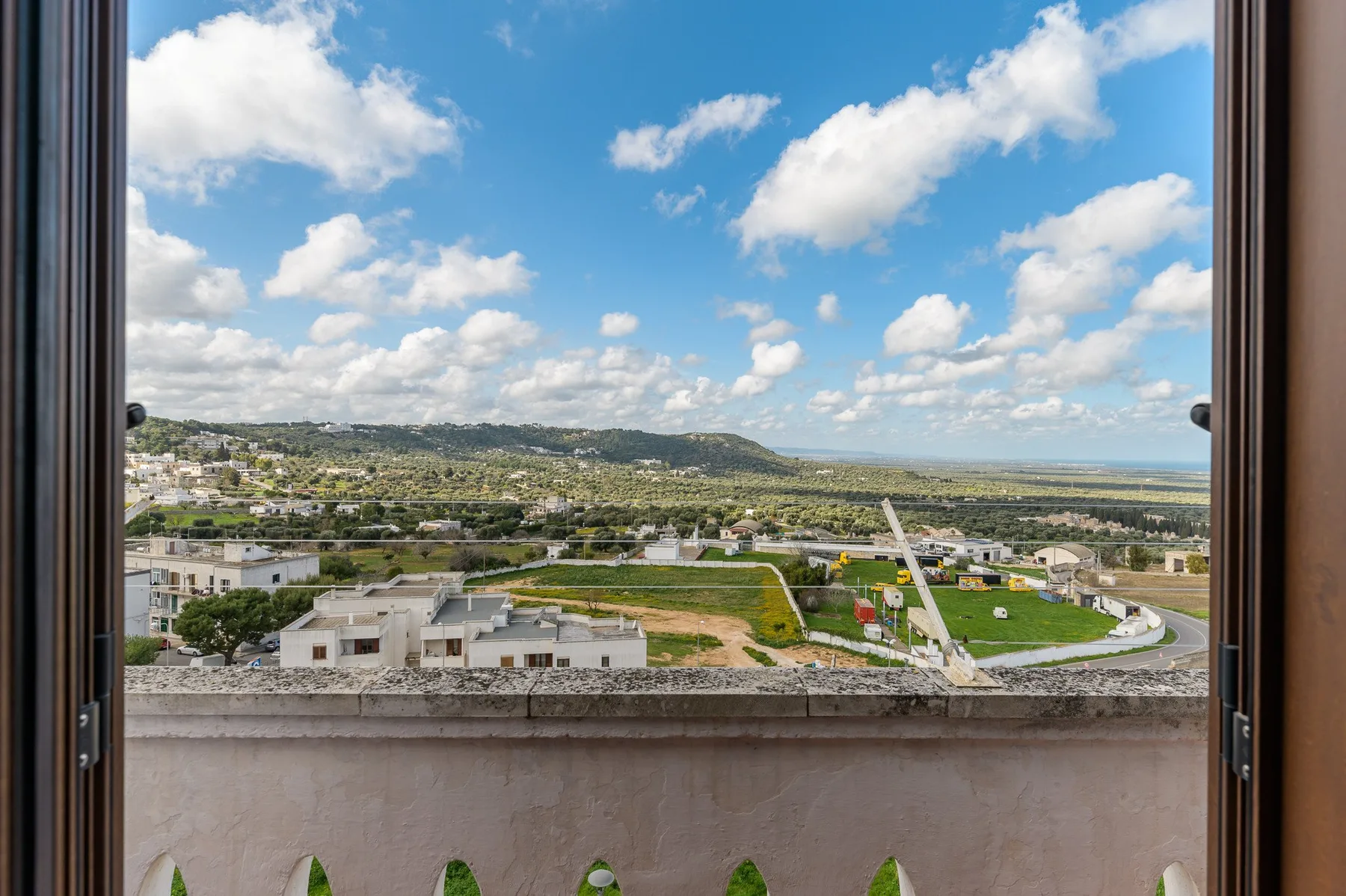 Vista desde un balcón hacia campos verdes y colinas lejanas bajo un cielo nublado.