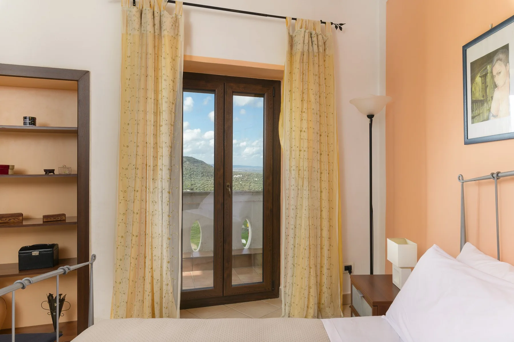 Un dormitorio con una cama junto a ventanas altas enmarcadas por cortinas.
