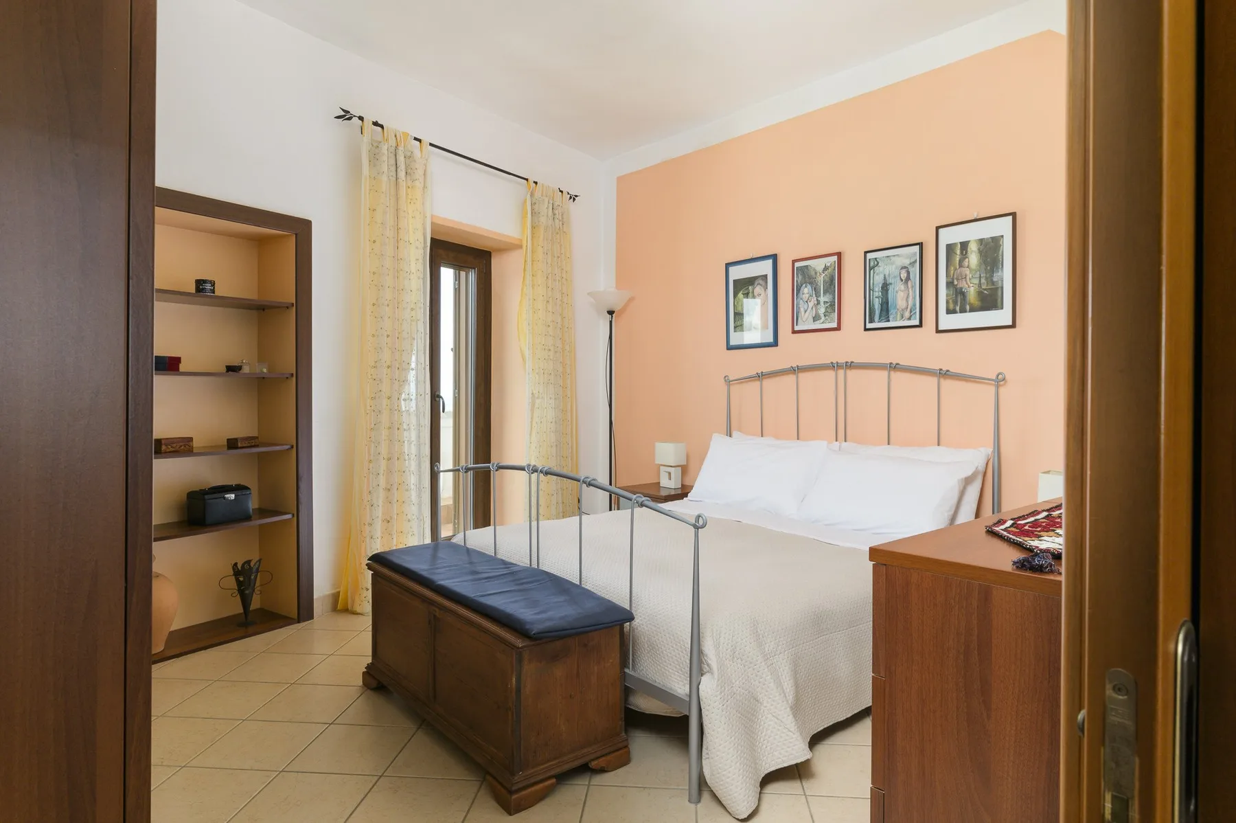 Un dormitorio con una cama, un banco de madera y cuadros en la pared.