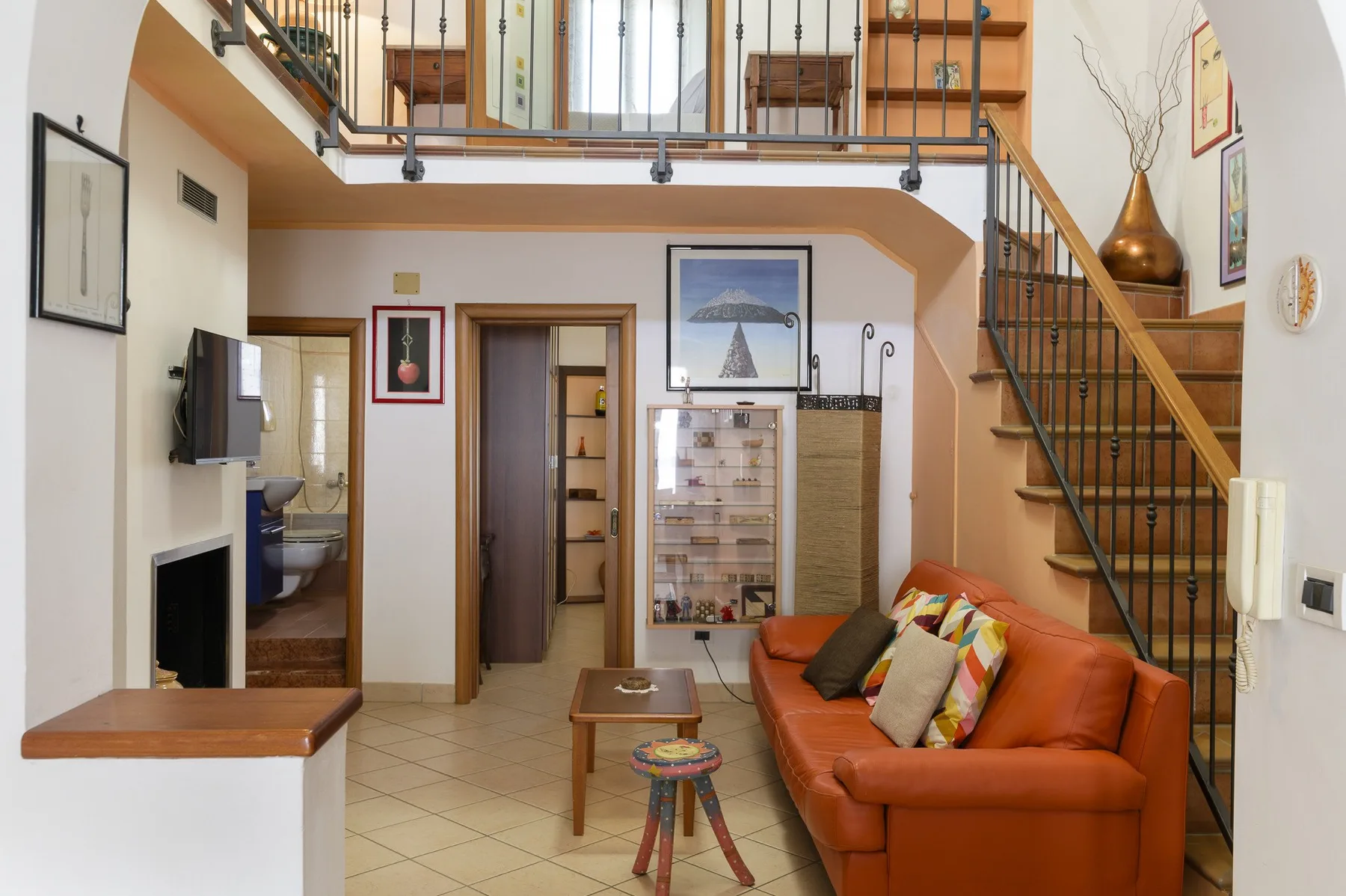 Una sala de estar con un sofá naranja bajo una escalera y una barandilla superior.