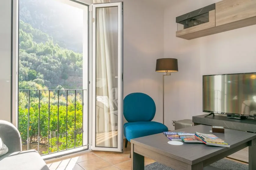 Una sala luminosa da a un balcón, con asientos azules y un televisor.