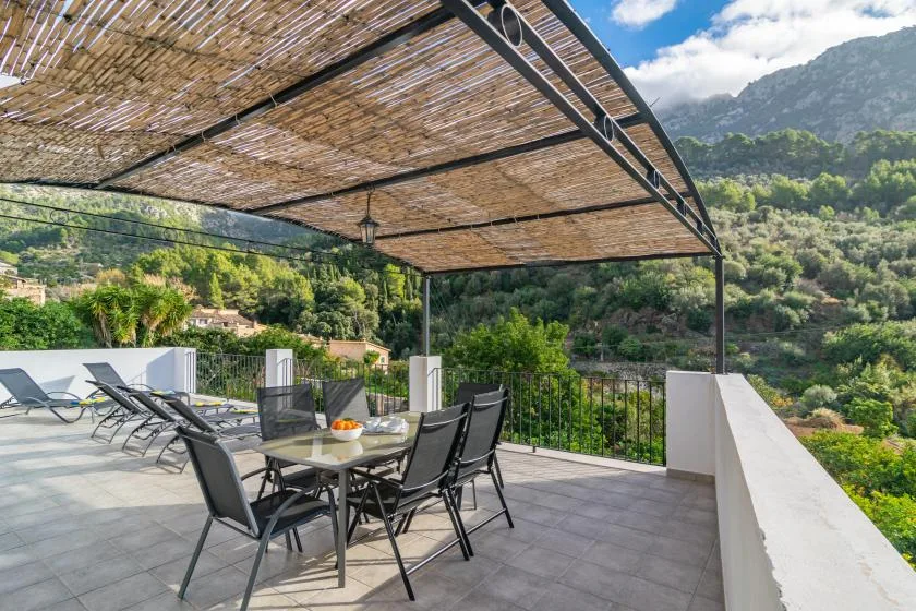 An outdoor terrace has a dining table and seating beneath a woven shade canopy.