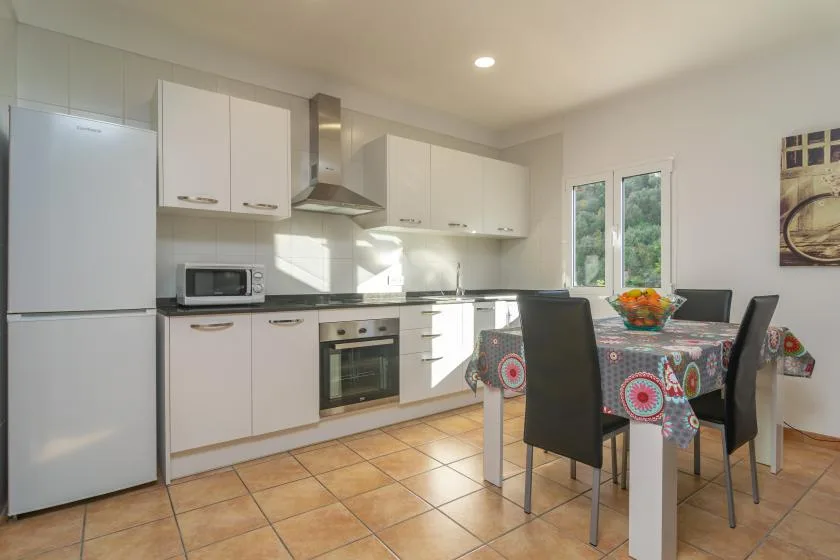 Una cocina luminosa con zona de comedor, armarios blancos y una mesa.